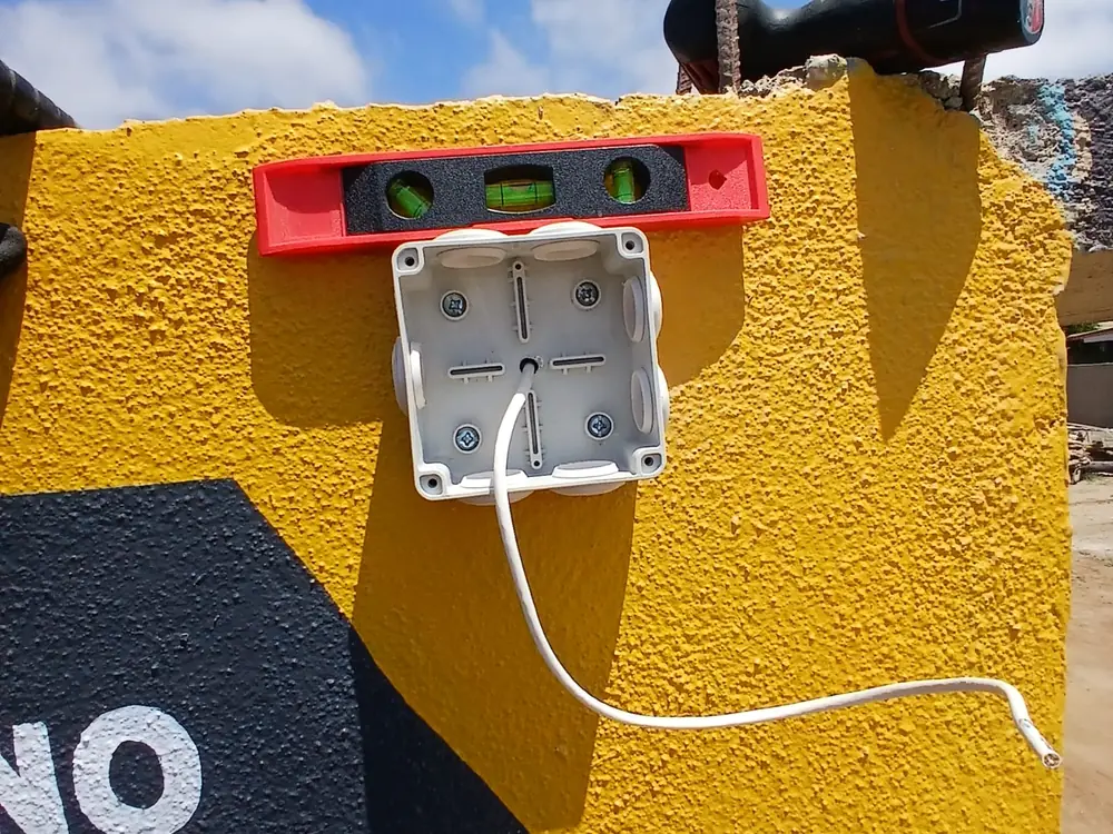 Caja de conexiones montada en muro con nivel de burbuja encima confirmando que está derecha